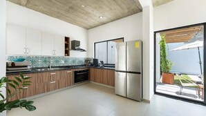 Eine moderne Küche mit Holzausstattung, einem Edelstahlkühlschrank und Blick ins Freie durch eine Glastür.