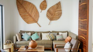 Ein Wohnzimmer mit einer Couch, einem Couchtisch und Sesseln. An der Wand befinden sich dekorative Blätter und auf dem Tisch eine Vase.