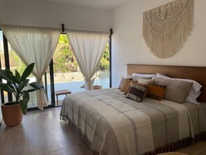 Une chambre avec un grand lit, une vue sur l’extérieur et une décoration murale en macramé.
