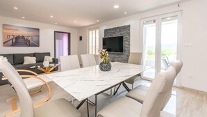 A modern living room with a large TV, a stone wall, and a dining area with a marble table.