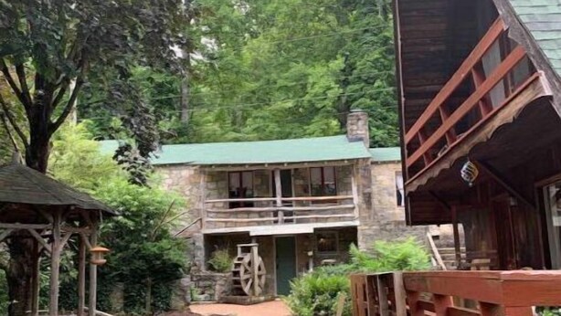 A rustic cabin with a stone exterior, a green roof, and a wooden deck. - Stone Cottage (Laurel Park)
