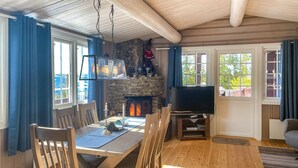 A cozy living room with a stone fireplace, a television, and a dining area with wooden furniture.