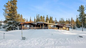 A wooden lodge with a covered porch and a snow-covered landscape.