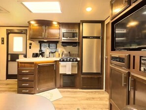 Kitchen features a central island with a sink, stove, and microwave, along with a refrigerator and dark wood cabinetry.