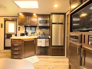 Kitchen features a central island with a sink, stove, and microwave, along with a refrigerator and dark wood cabinetry.