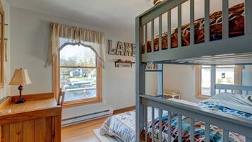 Habitación con literas y vistas a un puerto deportivo, un escritorio de madera con lámpara, y una estantería en la pared con adornos.