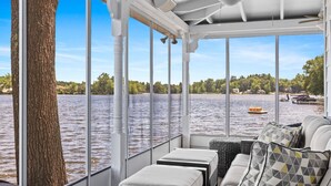 A boat interior with a large window overlooking a lake, a tree trunk, and a seating area with cushions.