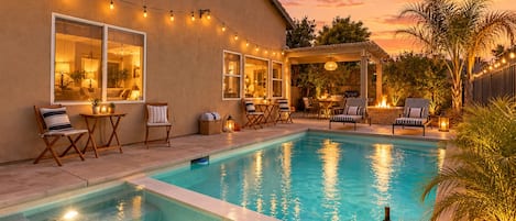 A backyard with a swimming pool, outdoor seating, and string lights.