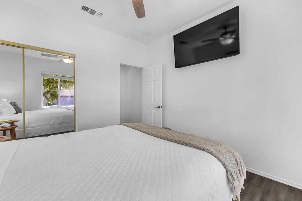 A bedroom with a bed, a mirror, a TV, and a door.