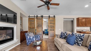 A living room with a fireplace, a ceiling fan, a sofa, a coffee table, and a sliding door leading to another room. - Luxe Villa On Golf Course 🏌️~ Private Pool/Spa 🏊 ~EV Charger ~ Tennis (Indio)