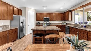 A kitchen with wooden cabinets, stainless steel appliances, granite countertops, and a central island with bar stools. - Luxe Villa On Golf Course 🏌️~ Private Pool/Spa 🏊 ~EV Charger ~ Tennis (Indio)