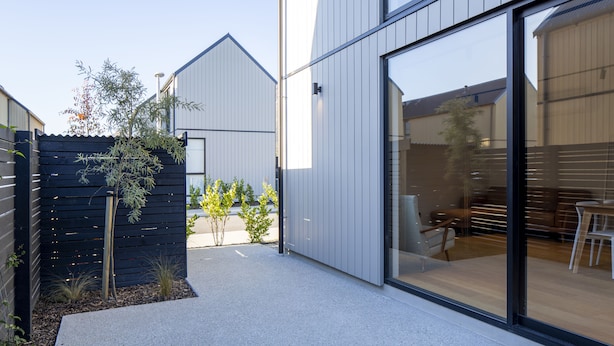 A modern building with large glass windows, a patio area with seating, and a small garden with plants. - Modern 3BR Home, Mountain View, Family Stay, Wi-Fi (Jacks Point)