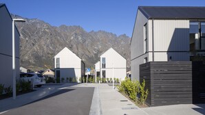 A modern building with a flat roof and large windows, surrounded by a mountain backdrop. - Modern 3BR Home, Mountain View, Family Stay, Wi-Fi (Jacks Point)