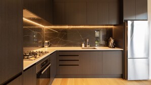 A modern kitchen with dark cabinetry, a marble backsplash, and stainless steel appliances. - Modern 3BR Home, Mountain View, Family Stay, Wi-Fi (Jacks Point)