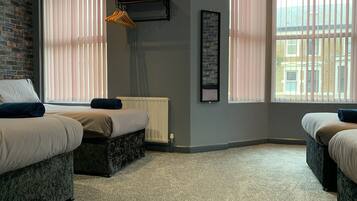 A hotel room with two beds, a radiator, a hanging coat rack, and a window with blinds.