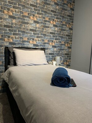 Una cama bien hecha con un edredón blanco, una toalla azul enrollada y un control remoto sobre la cama.