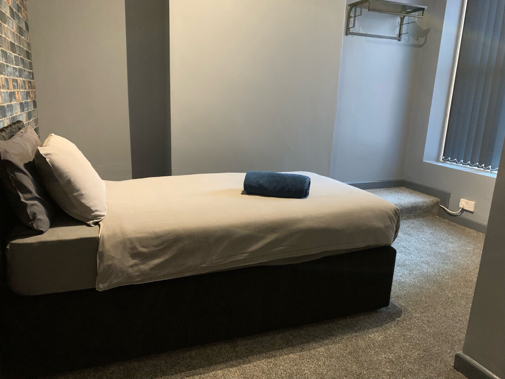 A small, neatly made bed with a dark headboard, a single pillow, and a folded blanket.