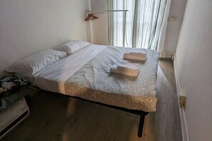 A single bed with a patterned bedspread, two folded towels, and a wooden hanger on the wall.