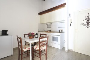 A compact kitchen with white cabinets, a wooden dining table with floral chairs, and a white refrigerator.