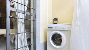 Een wasruimte met een wasmachine, een metalen hekwerk en een kleine lantaarn bovenop de machine.
