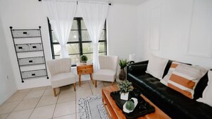 A living room with a black leather sofa, two white chairs, a wooden coffee table, and a black metal shelf unit. - Perfect Family Vacation House (Pace)