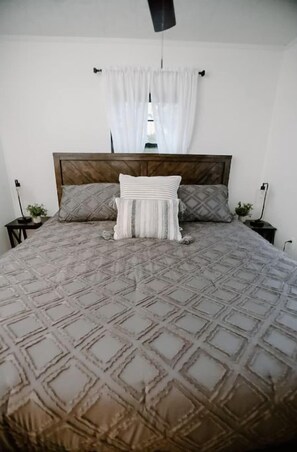Un lit bien fait, recouvert d’une couvre-lit à motifs, avec deux oreillers et un rideau blanc suspendu.