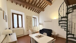 A room with a dining table, chairs, a sofa, a lamp, a radiator, and a spiral staircase. - S318 - Sirolo, wonderful three-room apartment in a historic building (Sirolo)