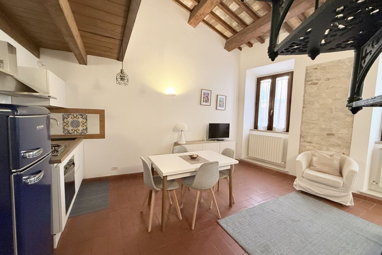 A compact kitchen with a refrigerator, stove, and dining table with chairs. There's a television and a window with a view.