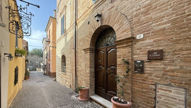 A narrow cobblestone street with a brick building featuring a large wooden door and potted plants. - S318 - Sirolo, wonderful three-room apartment in a historic building (Sirolo)