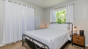 A bedroom with a bed, a nightstand, a window with curtains, and a lamp. - Tourists’ Haven~Clean~Centrally Located (Rapid City)