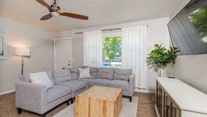 A living room with a grey sectional sofa, a wooden coffee table, a ceiling fan, a white lamp, a large window with curtains, and a potted plant. - Tourists’ Haven~Clean~Centrally Located (Rapid City)