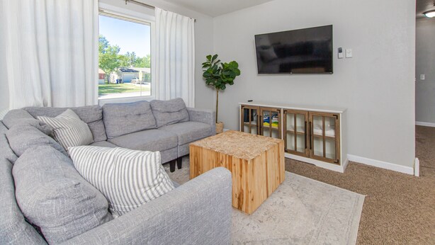 A living room with a grey sectional sofa, a wooden coffee table, a TV mounted on the wall, and a plant. - Tourists’ Haven~Clean~Centrally Located (Rapid City)