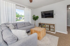A living room with a grey sectional sofa, a wooden coffee table, a TV mounted on the wall, and a plant. - Tourists’ Haven~Clean~Centrally Located (Rapid City)