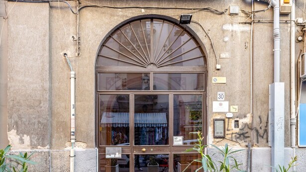 Une devanture de magasin avec une grande fenêtre en arc de cercle, un panneau indiquant clairement le numéro « 30 », et un petit espace extérieur aménagé avec des tables et des chaises.