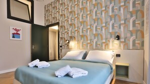 Une chambre d’hôtel avec un lit, une table de chevet, un mur orné d’un motif géométrique et une porte.