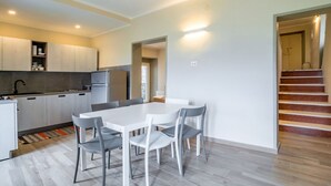 Une cuisine moderne avec des meubles blancs, une table à manger avec des chaises et un escalier menant à un autre niveau.