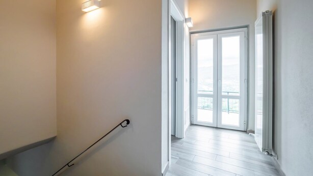 Un couloir avec une main courante, une porte donnant sur un balcon et un luminaire fixé au mur.