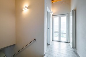 Un couloir avec une main courante, une porte donnant sur un balcon et un luminaire fixé au mur.