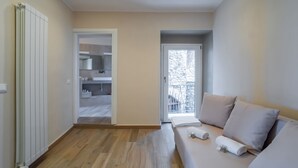 Une chambre moderne avec un plancher en bois, un canapé avec des coussins, un radiateur et une porte donnant sur un balcon.