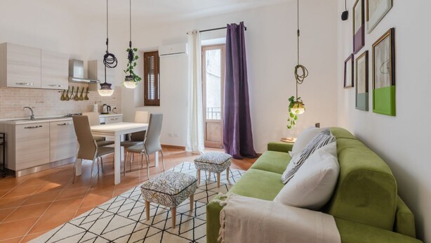 A modern kitchen with a dining area, a green sofa, and a window with purple curtains.