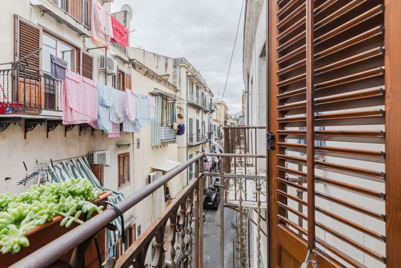 A narrow alleyway with buildings on either side, balconies with laundry, and a metal gate.