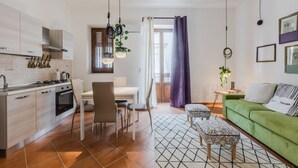A modern kitchen with a dining area, a green sofa, and a patterned rug.