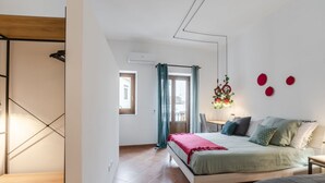 A bedroom with a bed, a desk, a chair, a window with curtains, and a wall-mounted plant.
