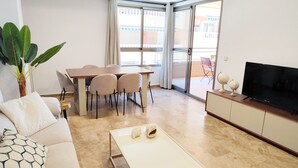 Ein Wohnzimmer mit Sofa, Couchtisch, Fernseher, Esstisch mit Stühlen und einer Glastür zum Außenbereich.