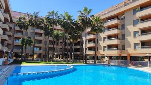 Ein Swimmingpool, umgeben von Palmen und einem mehrstöckigen Gebäude mit Balkonen.