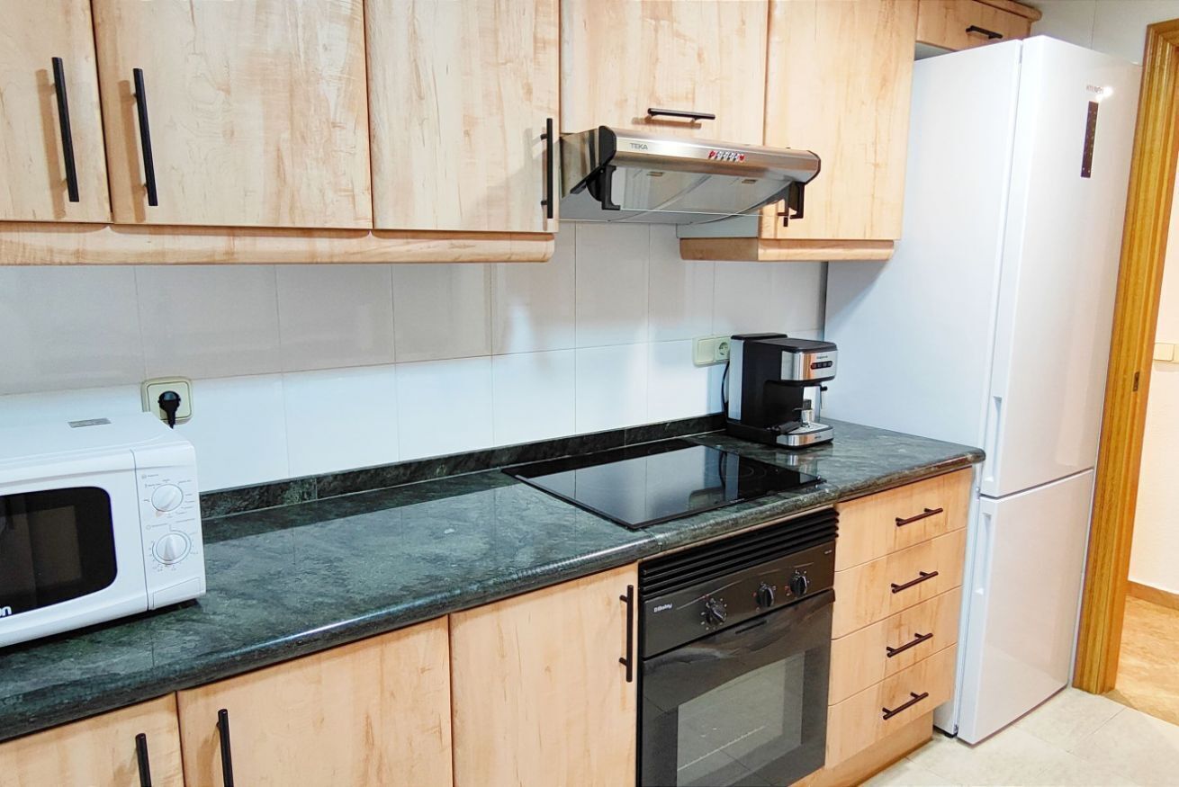 Eine Küche mit Holzausstattung, einer Mikrowelle, einer Kaffeemaschine, einem Herd und einem Kühlschrank.