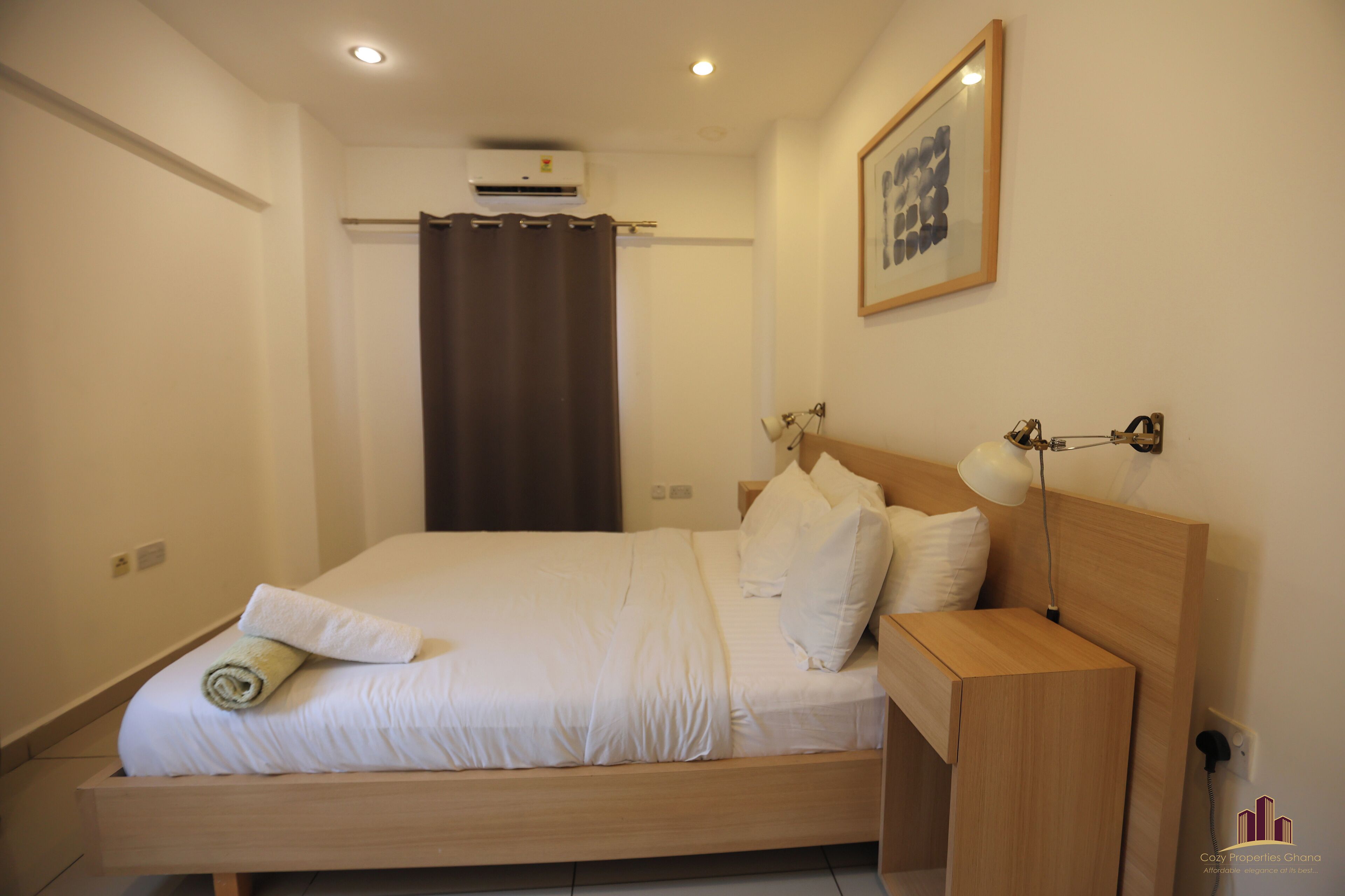 A neatly made bed with white linens, a wooden headboard, and a bedside table with a lamp.