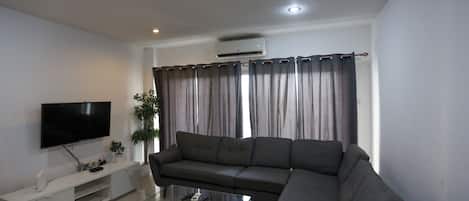 A modern living room with a flat-screen TV, a grey sofa, a glass coffee table, and a white entertainment unit.