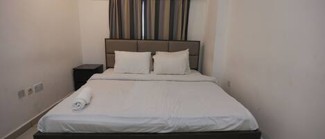 A neatly made bed with a dark headboard, a small bedside table, and a wall-mounted air conditioner.