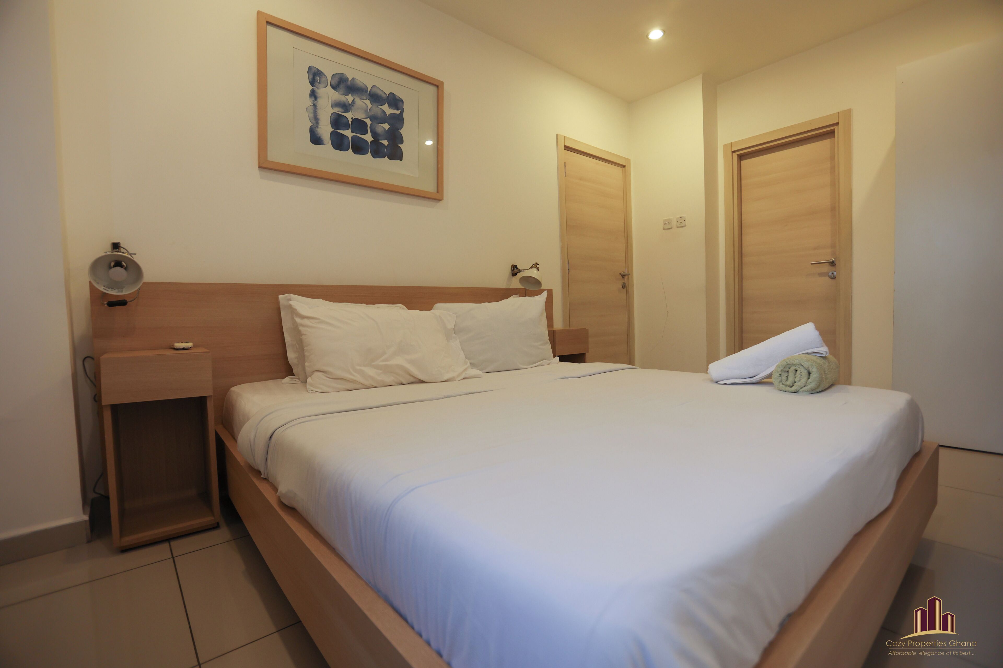 Een net opgemaakt bed met witte lakens, een houten hoofdbord en een lijstwerk erboven.